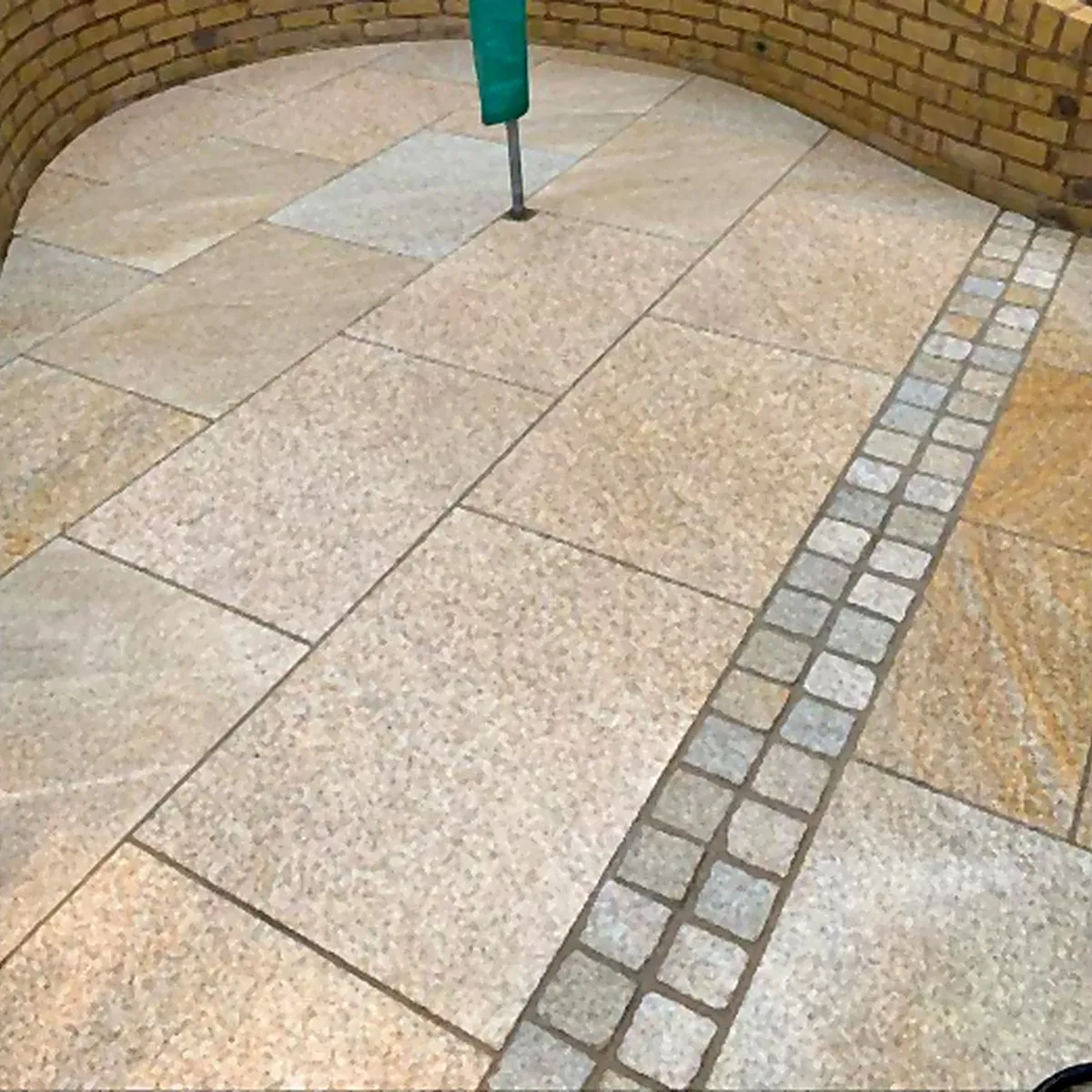 Dieselbe Terrasse nach der Reinigung: goldfarben gemaserter Granit, der Pflasterstreifen hebt sich hell ab